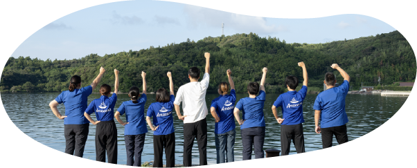 水辺を背景に右手を空に掲げるAmacareスタッフの集合写真